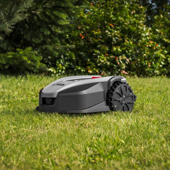 Grå robotplæneklipper kører på en græsplæne foran en mørkegrøn hæk